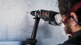 Una persona che indossa un equipaggiamento di sicurezza pratica un foro in un muro di cemento.