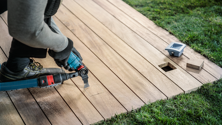 Una persona che indossa dispositivi di sicurezza taglia un ponte di legno con un utensile elettrico.