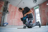 Una persona che indossa un equipaggiamento di sicurezza perfora un pavimento di cemento con un martello perforatore a batteria.