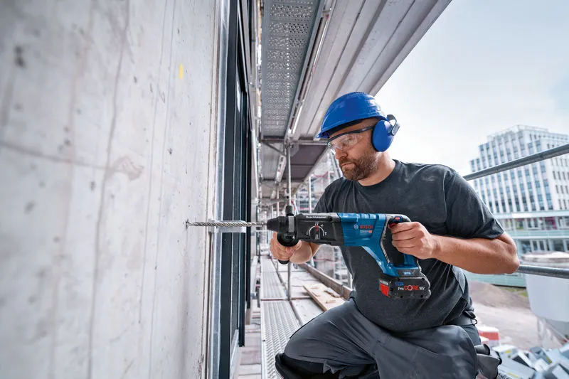 Una persona che indossa un equipaggiamento di sicurezza perfora un muro di cemento con un martello perforatore.