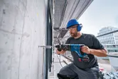 Una persona che indossa un equipaggiamento di sicurezza perfora un muro di cemento con un martello perforatore.