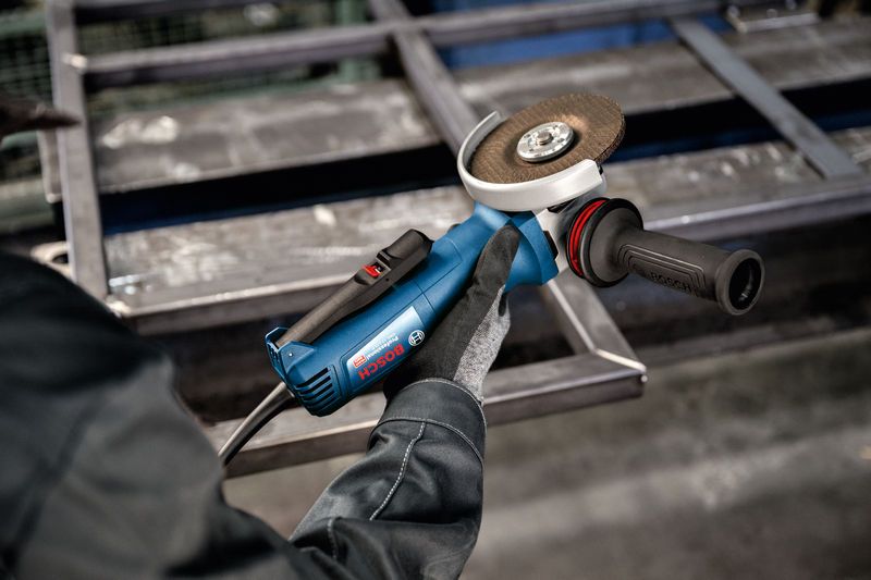 Una persona che indossa dispositivi di sicurezza utilizza una smerigliatrice angolare vicino a un telaio metallico.