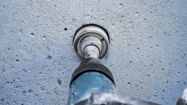 Un martello perforatore pratica un grande foro in un muro di cemento.