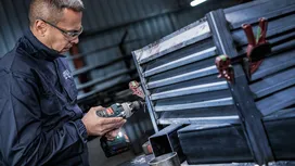 Una persona che indossa un equipaggiamento di sicurezza fora un telaio di ventilazione in metallo in un'officina.