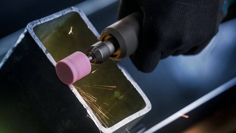 Una persona che indossa un equipaggiamento di sicurezza leviga il bordo di un tubo metallico con un utensile rotante.