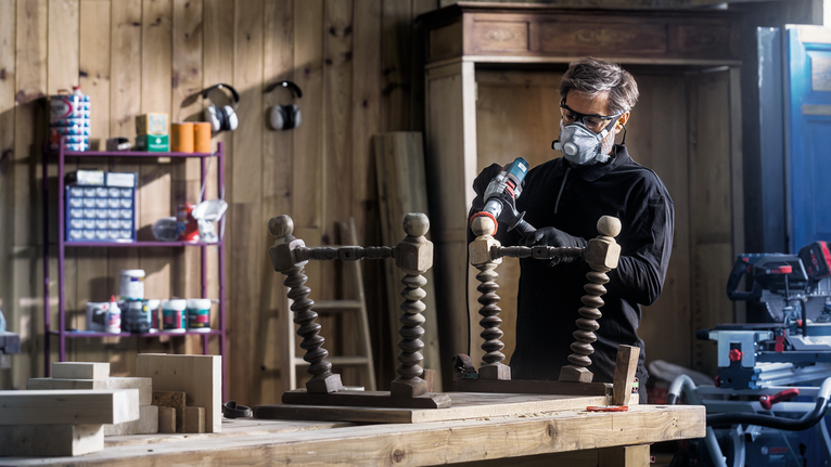 Una persona che indossa dispositivi di sicurezza perfora un tavolo di legno capovolto in un'officina.