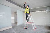 Una persona che indossa dispositivi di protezione individuale segna il soffitto utilizzando una livella laser.