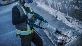 Una persona che indossa un equipaggiamento di sicurezza utilizza un martello demolitore per rompere il cemento.