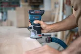 Una persona utilizza una fresatrice per legno a batteria con sistema di aspirazione della polvere su un piano di lavoro.