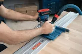 Una persona guida una fresatrice a batteria lungo una guida su una superficie di legno.