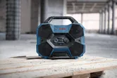 Una radio da cantiere dal design robusto è appoggiata su assi di legno in un'area di costruzione.