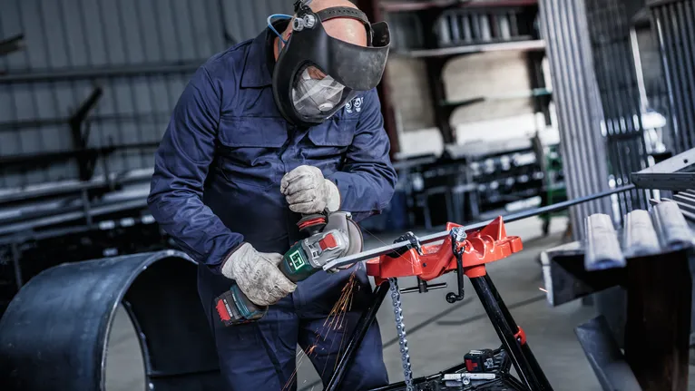Una persona che indossa un equipaggiamento di sicurezza utilizza una smerigliatrice angolare per tagliare il metallo, producendo scintille.