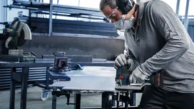 Una persona che indossa dispositivi di sicurezza taglia la lamiera con un elettroutensile in un'officina.