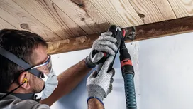 Una persona che indossa un equipaggiamento di sicurezza utilizza un elettroutensile per levigare una trave di legno.