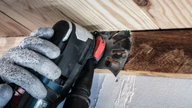 Una persona che indossa dispositivi di sicurezza taglia la legna con un utensile multiuso vicino al soffitto.