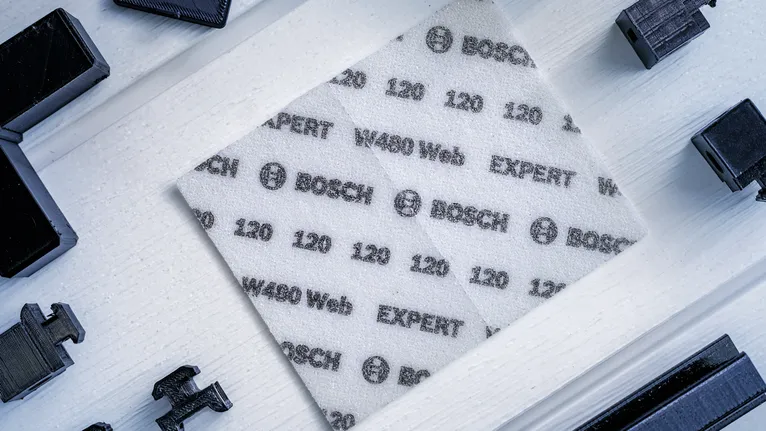 Un foglio abrasivo bianco con le specifiche stampate viene posizionato su una superficie di legno chiaro.