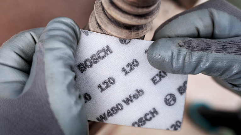 Una persona che indossa un equipaggiamento di sicurezza tiene un tampone abrasivo vicino a un tubo metallico.