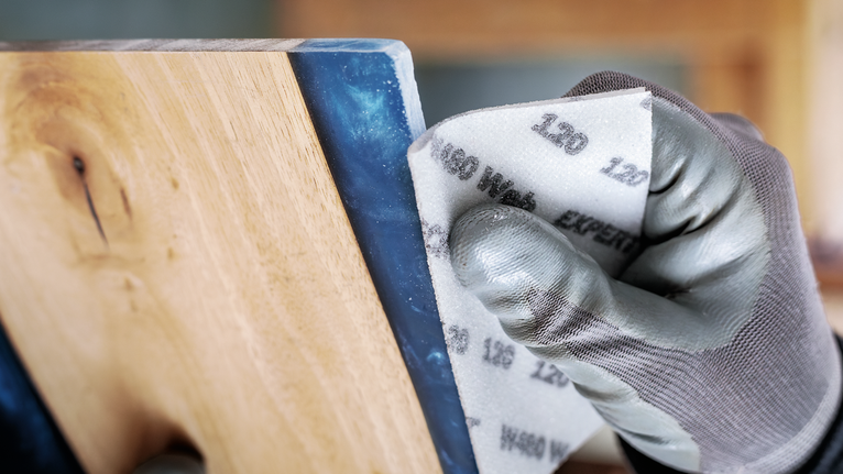 Persona che indossa dispositivi di sicurezza mentre leviga una superficie di legno.