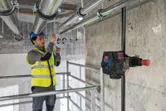 Una persona che indossa dispositivi di sicurezza allinea i tubi utilizzando uno strumento di livellamento laser.