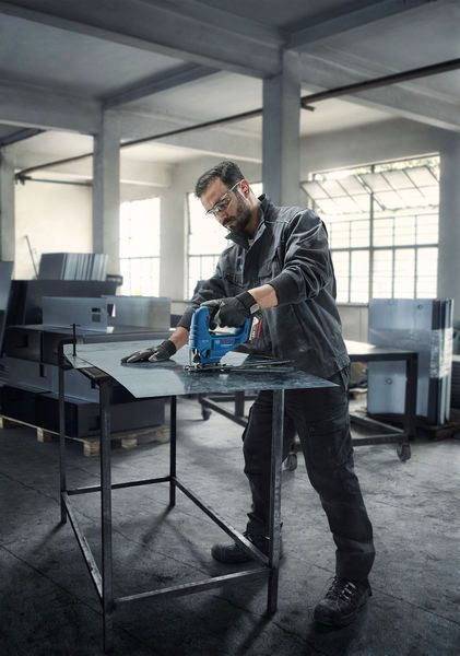 In un'officina, una persona con indosso dispositivi di protezione individuale taglia una lamiera con un utensile elettrico.
