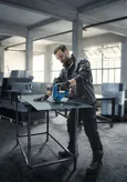 In un'officina, una persona con indosso dispositivi di protezione individuale taglia una lamiera con un utensile elettrico.