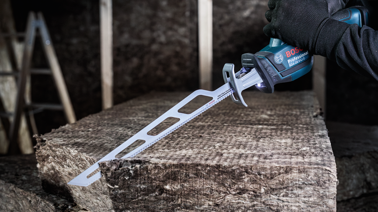 Una persona che indossa un equipaggiamento di sicurezza utilizza un seghetto alternativo per tagliare il materiale isolante.