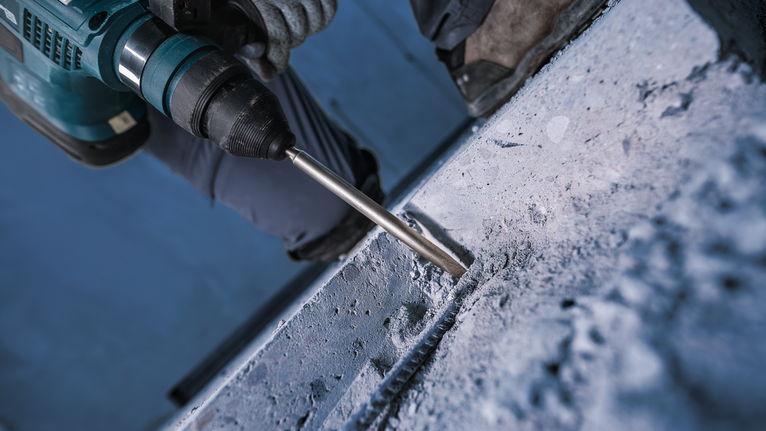 Una persona che indossa dispositivi di sicurezza utilizza un martello perforatore sul calcestruzzo.