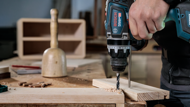 Una persona pratica un foro in assi di legno in un'officina.