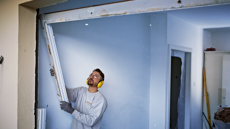 Una persona che indossa un equipaggiamento di sicurezza rimuove lo stipite di una porta all'interno di un edificio.
