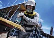 Una persona che indossa dispositivi di sicurezza taglia il legno con un seghetto alternativo in un cantiere edile.