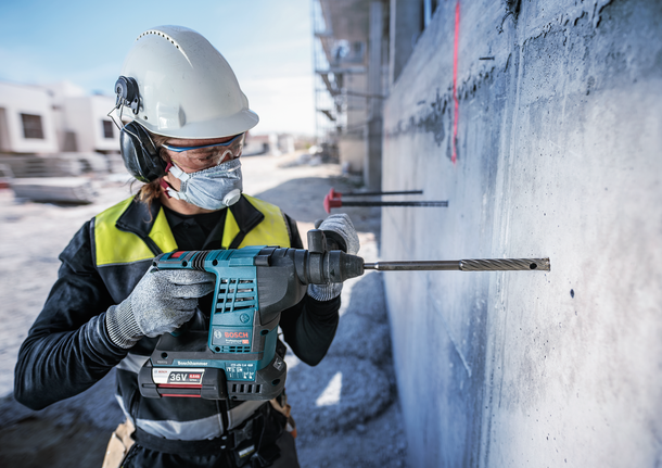 Una persona che indossa un equipaggiamento di sicurezza fora un muro di cemento in un cantiere edile.