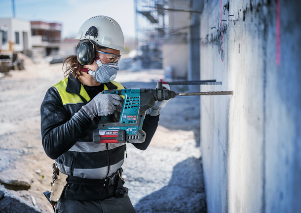Una persona che indossa un equipaggiamento di sicurezza fora un muro di cemento in un cantiere edile.