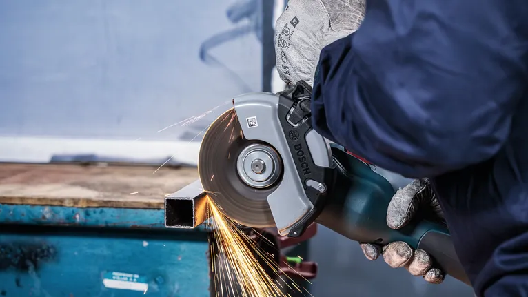 Una persona che indossa un equipaggiamento di sicurezza taglia un tubo di metallo utilizzando una smerigliatrice angolare.
