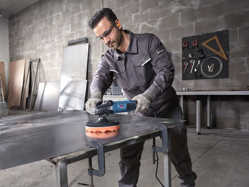 Una persona che indossa un equipaggiamento di sicurezza lucida una lamiera con un utensile elettrico.