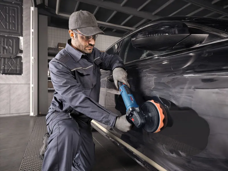 Una persona che indossa un equipaggiamento di sicurezza lucida un'auto nera utilizzando un utensile elettrico.