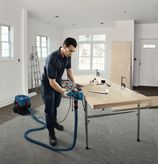 Una persona che indossa un equipaggiamento di sicurezza utilizza una pialla su una tavola di legno in un'officina.