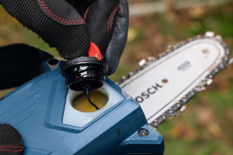 Una persona che indossa dispositivi di sicurezza apre il tappo dell'olio vicino alla lama di un potatore a batteria.