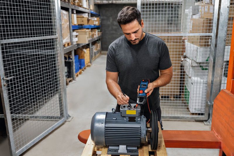 Persona che testa un motore industriale con una pinza amperometrica in un magazzino.