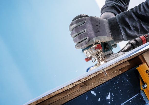 Un lavoratore che indossa dispositivi di sicurezza utilizza un seghetto alternativo per tagliare un pezzo di legno laminato.