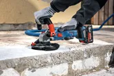 Una persona che indossa dispositivi di sicurezza leviga il calcestruzzo con una smerigliatrice a batteria.