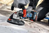 Una persona che indossa dispositivi di sicurezza utilizza una levigatrice per calcestruzzo senza fili su una superficie del pavimento.