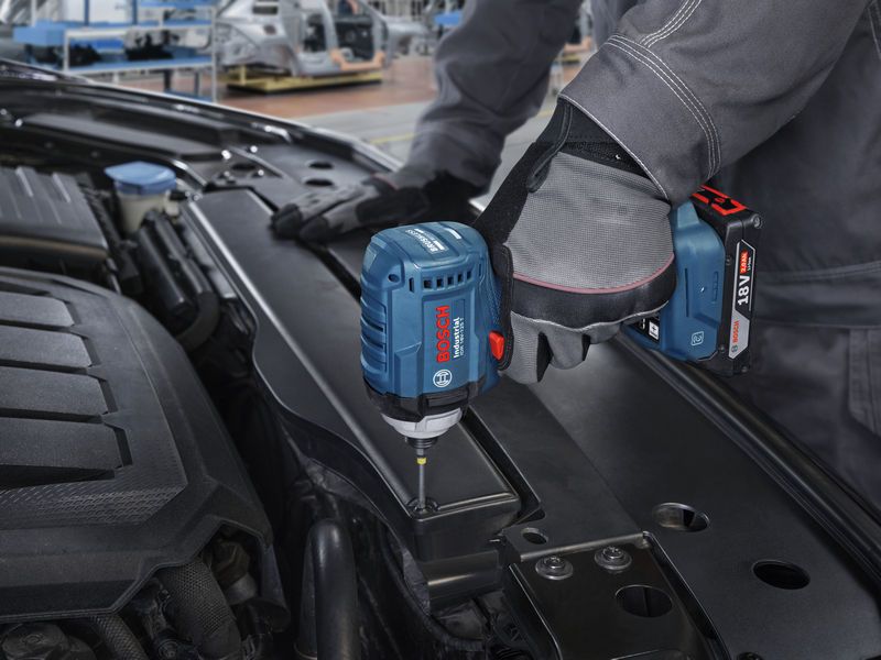 Una persona che indossa un equipaggiamento di sicurezza utilizza un avvitatore a impulsi per avvitare una vite nel vano motore di un'auto.