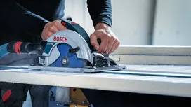 Una persona usa una sega circolare per tagliare una grande piastrella su un banco da lavoro.