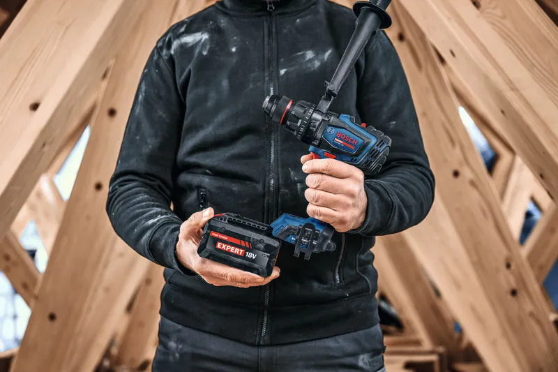 Una persona che indossa un equipaggiamento di sicurezza tiene in mano un trapano combinato a batteria e una batteria.