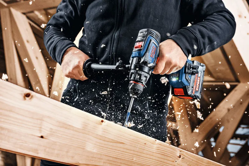 Una persona usa un trapano a batteria per forare una trave di legno.