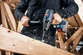 Una persona usa un trapano a batteria per forare una trave di legno.