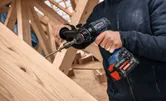 Una persona usa un trapano avvitatore a batteria per avvitare una vite su travi di legno.