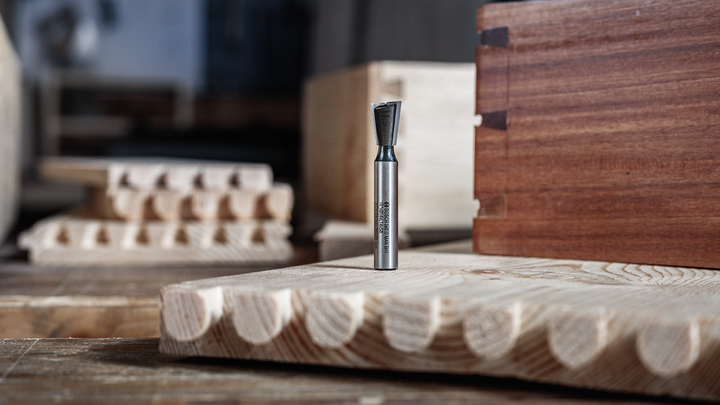 Fresa a coda di rondine appoggiata su una tavola di legno, con giunti intagliati visibili.