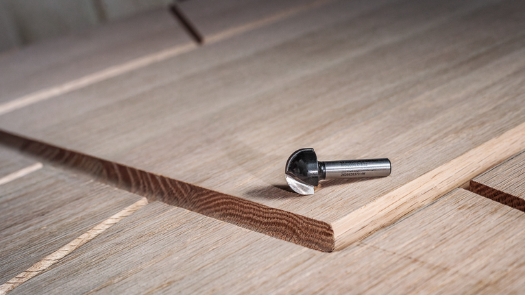 Fresa in metallo duro appoggiata su un pannello di legno stratificato con una scanalatura appena tagliata.