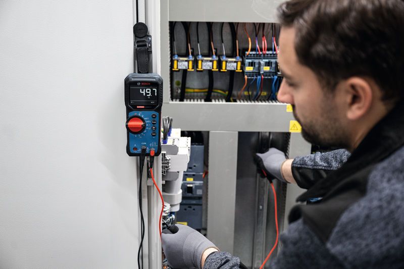Una persona che indossa un equipaggiamento di sicurezza utilizza un multimetro digitale per testare un quadro elettrico.